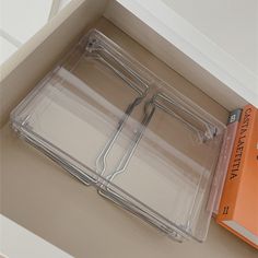 two clear plastic trays sitting on top of a white counter next to an orange book