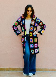 a woman standing in front of a pink wall wearing a black crocheted cardigan