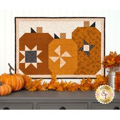 a table with some pumpkins on it and a quilted wall hanging in the background