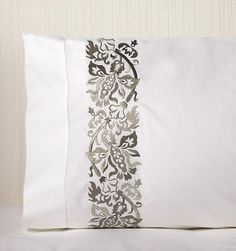 an embroidered pillow on a bed with white sheets and pillows in front of a wall