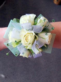 a bridal bouquet with white roses and green leaves on someone's arm in a parking lot