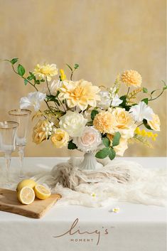 a vase filled with yellow and white flowers on top of a table next to two glasses