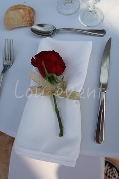 a single red rose is placed on a napkin next to silverware and utensils