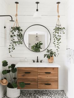 a bathroom with white walls and wooden cabinets, plants on the wall, and a round mirror