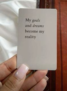 a person holding up a card that says, my goals and dreams become my reality