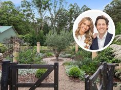 a man and woman standing in front of a garden with trees, shrubs and bushes