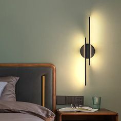 a bed sitting under a wall light next to a night stand with a lamp on it