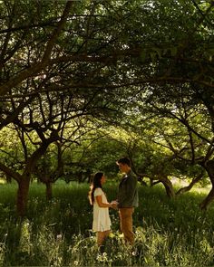 a man and woman standing in tall grass under trees