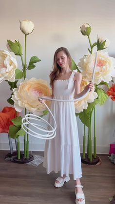 a woman in a white dress standing next to flowers and holding a large object with one hand