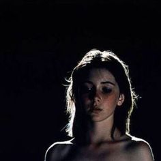 a woman is standing in the dark with no shirt on and her eyes are half closed