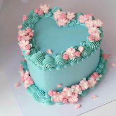 a blue heart shaped cake with pink flowers on the top and bottom, sitting on a white surface