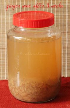 a glass jar filled with liquid sitting on top of a red table cloth next to a wall