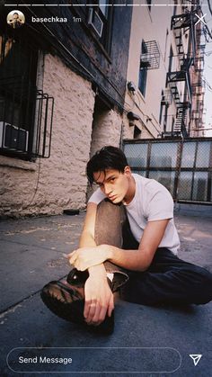 a young man sitting on the ground with his hand on his knee and looking down