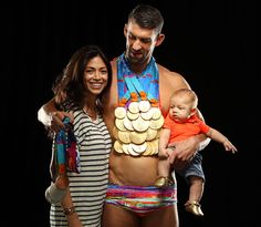 a man and woman holding a baby in front of a black background with gold coins on his chest