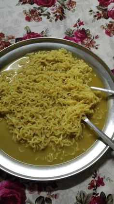 there is noodle soup in the bowl on the table with spoons and flowers