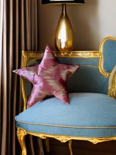 a pink star pillow sitting on top of a blue chair next to a gold lamp