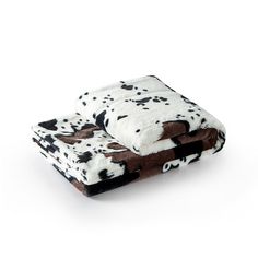 a cow print blanket sitting on top of a white floor next to a black and brown pillow