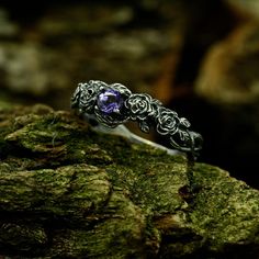 a silver ring with an amethorate stone in the center on top of mossy rocks