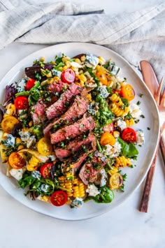 steak and corn salad on a white plate with silverware next to it, along with utensils