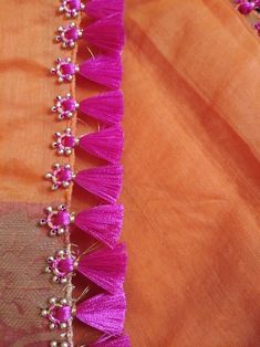 an orange and pink saree with beads on the border is seen in closeup