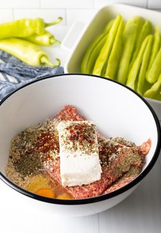 a white bowl filled with meat and seasoning next to green peppers