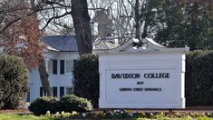 the sign for davidson college in front of a white building with trees and bushes around it