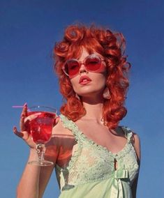 a woman with red hair and sunglasses holding a drink