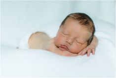 a newborn baby is sleeping on a white blanket with his eyes closed and head turned to the side