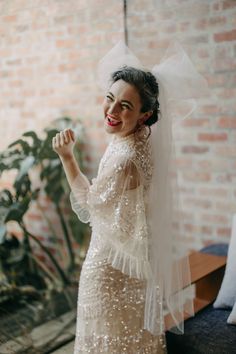 a woman in a wedding dress standing next to a brick wall and smiling at the camera