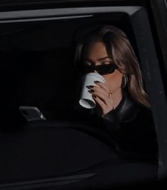 a woman sitting in the back seat of a car drinking out of a coffee cup