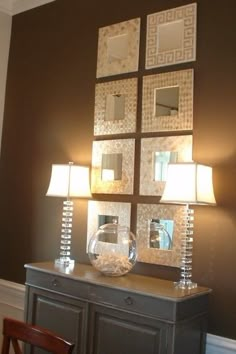 a table with two lamps and pictures on the wall above it in a room that has dark brown walls