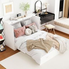 a white bed with pillows and blankets on top of it in a room next to a desk