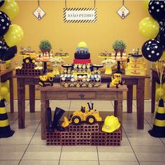 a table topped with lots of yellow and black balloons next to construction themed desserts