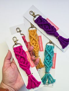 a hand holding three different colored crochet tassels in front of each other