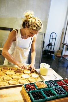 a woman in an apron making pies on a table with fruit and other ingredients