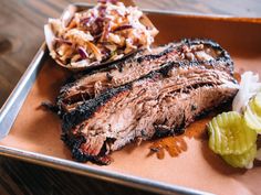 a steak and coleslaw on a plate with pickles in the foreground