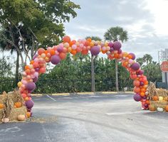 an arch made out of hay and balloons in the middle of a parking lot with pumpkins on it