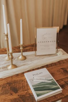 a wooden table topped with two candles and a book