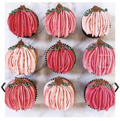 cupcakes decorated with pink frosting and green leaves on top of a marble surface