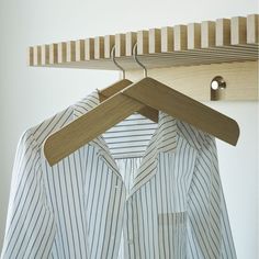 a shirt hanging on a wooden hanger next to a white wall with a striped shirt