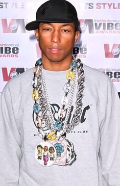 a young man wearing a black hat and some necklaces on his neck is standing in front of a white wall