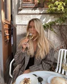 a woman sitting at an outdoor table with food and wine in her hand while holding a glass of wine