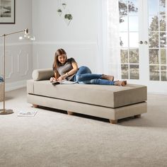 a woman laying on top of a couch in a living room next to a lamp