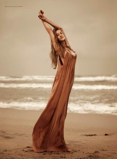 a woman is standing on the beach with her arms in the air and looking up