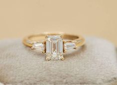 an emerald and baguette diamond ring on top of a white stone block in front of a beige background