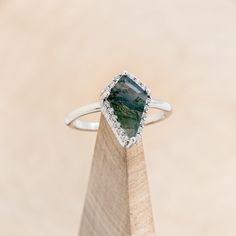 a ring with a large green stone in the middle on top of a wooden stand