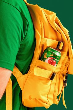 a person wearing a green shirt and yellow backpack with a can in it's pocket