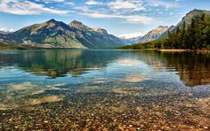 a lake surrounded by mountains and trees under a blue sky