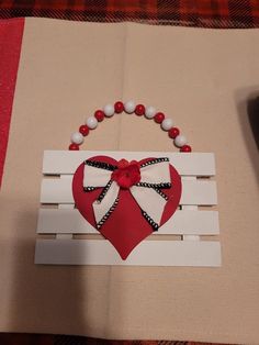 a red and white heart is hanging on a piece of wood with beads around it