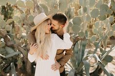 a man and woman embracing in front of cactus